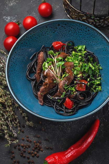 Macarrão preto com carne e tomate seco em um prato azul sobre uma mesa de pedra escura