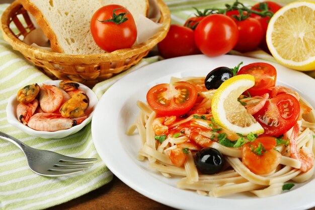 Macarrão saboroso com azeitonas pretas de mexilhões de camarões e molho de tomate na placa no fundo de madeira