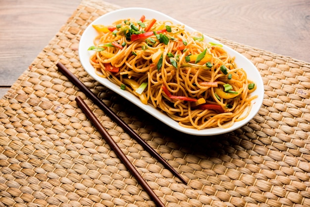 Macarrão Schezwan ou macarrão Hakka vegetal ou chow mein são receitas indo-chinesas populares, servidas em uma tigela ou prato com pauzinhos de madeira. foco seletivo