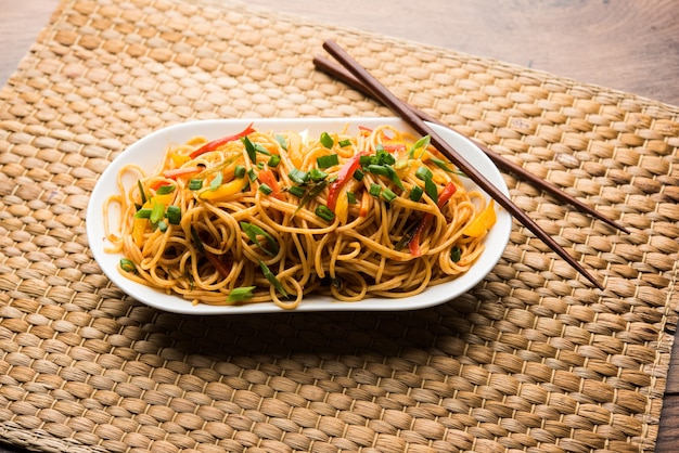 Macarrão Schezwan ou macarrão Hakka vegetal ou chow mein são receitas indo-chinesas populares, servidas em uma tigela ou prato com pauzinhos de madeira. foco seletivo