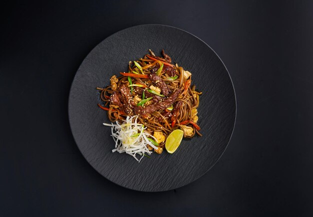 Macarrão soba com legumes e carne em macarrão preto sobre um fundo escuro