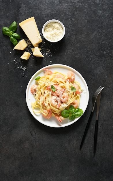 Macarrão tagliatelle com molho cremoso, parmesão e camarão em um prato sobre fundo preto. Vista de cima.