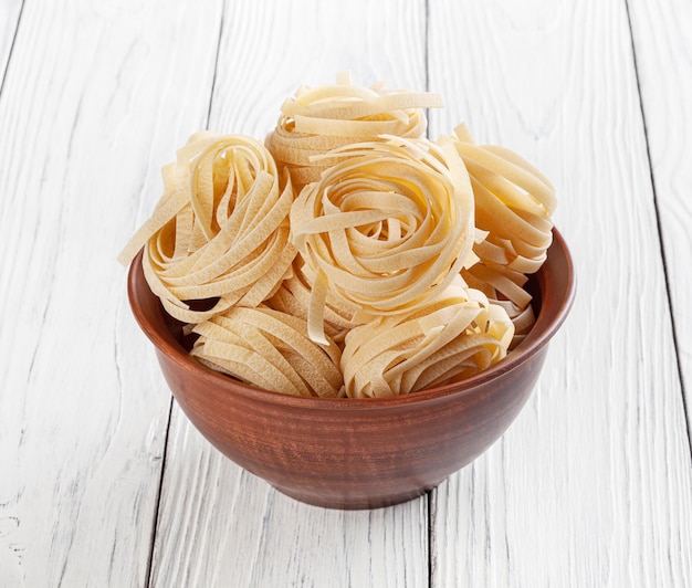 Macarrão tagliatelle cru em tigela de cerâmica sobre fundo branco de madeira