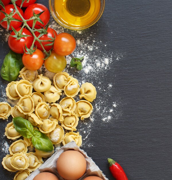 Foto macarrão tortellini fresco e ingredientes em um quadro escuro com espaço de cópia