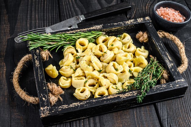 Macarrão tortellini tradicional italiano com espinafre em uma bandeja de madeira. fundo de madeira preto. vista do topo.