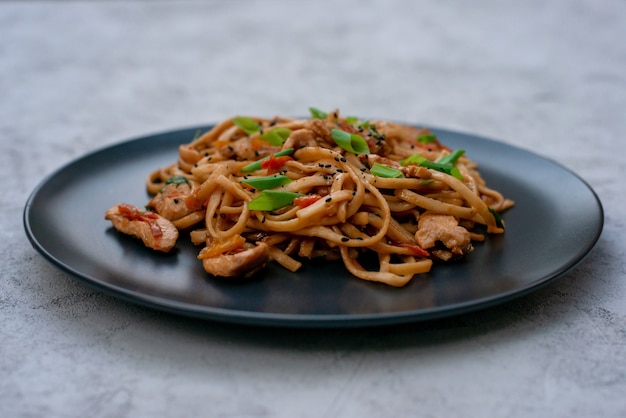 Macarrão udon asiático com legumes da galinha e molho teriyaki em um fundo preto de madeira