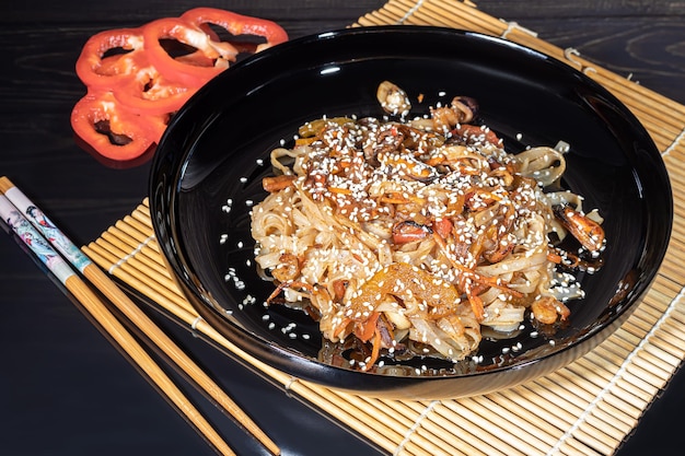 Macarrão udon com cogumelos de carne e legumes polvilhados com sementes de gergelim comida asiática assada em fundo preto