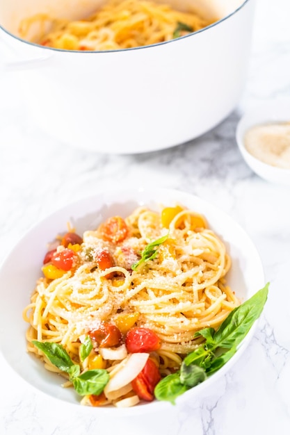 Macarrão vegetariano com tomate cereja e manjericão fresco em um prato branco.