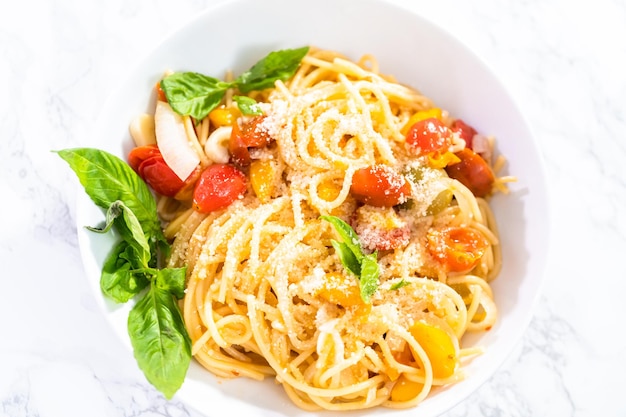 Macarrão vegetariano com tomate cereja e manjericão fresco em um prato branco.