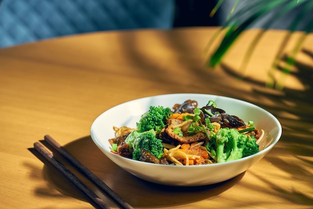 Macarrão wok com carne, vegetais, molho agridoce e pimenta Sichuan. Fundo de madeira. cozinha chinesa