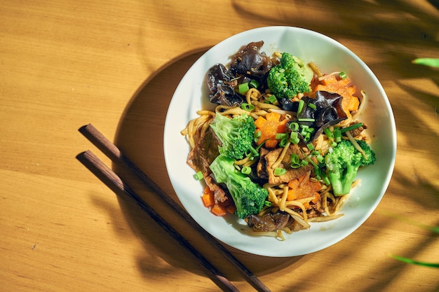 Macarrão wok com carne, vegetais, molho agridoce e pimenta Sichuan. Fundo de madeira. cozinha chinesa