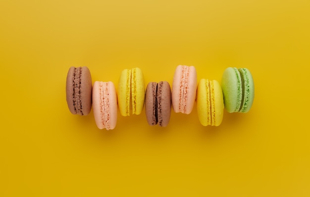 Foto macarrón. macarrón de pastel colorido con tonos pastel no apilados uniformemente en una fila sobre un fondo amarillo. vista superior de galletas de almendra.