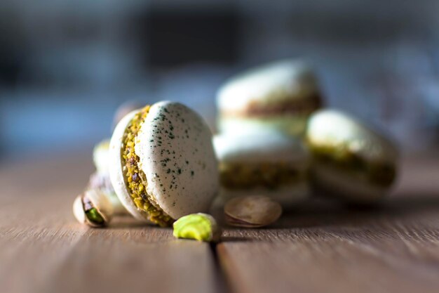 Macarrones caseros de pistacho y chocolate apilados en una mesa de madera con pistachos