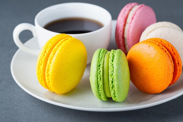 Macarrones de color francés con una taza de café blanca sobre fondo gris