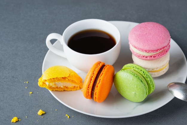 Macarrones de color francés con una taza de café blanca sobre fondo gris