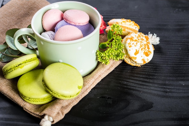 Macarrones de colores dulces en composición con flores sobre fondo negro. copia espacio