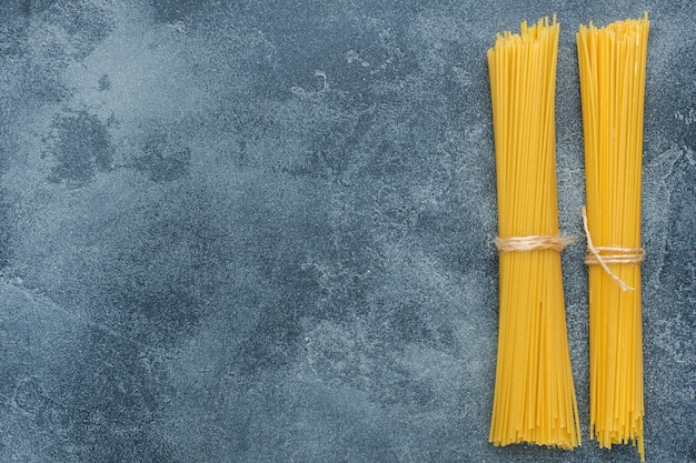 Macarrones crudos, espaguetis en una tabla de piedra oscura con el espacio de la copia. Pasta italiana casera.