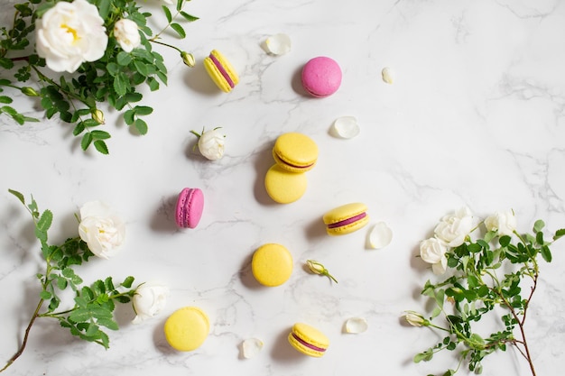 Macarrones y flores Comida francesa Macarrones amarillos y rosas sobre una mesa de mármol Postre francés