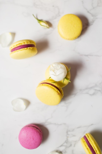 Macarrones y flores Comida francesa Macarrones amarillos y rosas sobre una mesa de mármol Postre francés