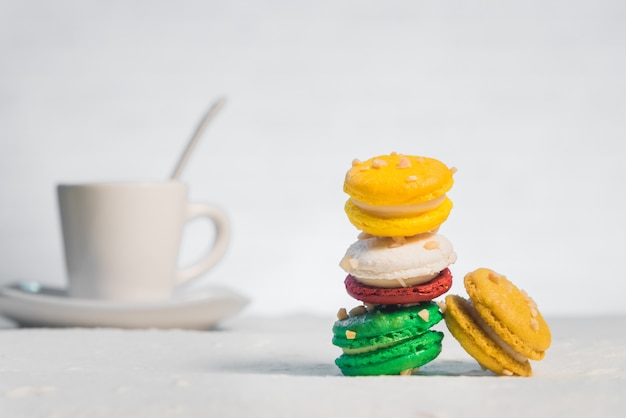 Macarrones franceses coloridos con la taza de café en el fondo blanco