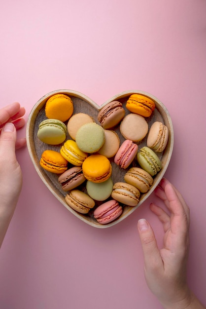 Macarrones galletas coloridas en un tazón de corazón de madera Macarons postre dulce francés vista superior fondo rosa Copiar espacio