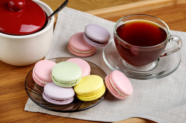 Macarrones multicolores y una taza de té en una bandeja de madera