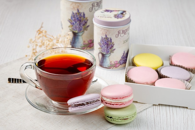 Macarrones multicolores y una taza de té en una mesa de cocina de madera clara Té de la mañana y dulces