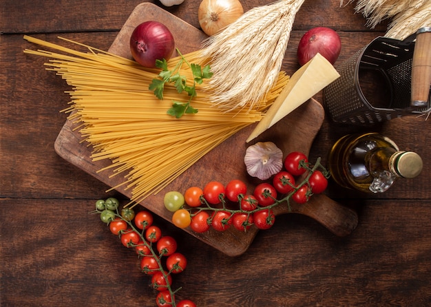 Macarrones de pasta italiana, espaguetis, tomates, aceite de oliva, queso y especias en madera rústica, vista superior.