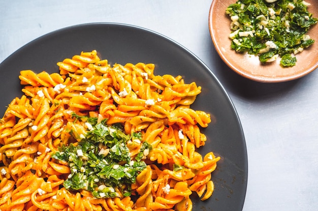 Foto macarrones de pasta rizada con salsa de tomate y gremolata en un plato oscuro redondo sobre una mesa