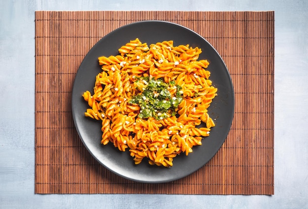 Macarrones de pasta rizada con salsa de tomate y gremolata en un plato oscuro redondo sobre una mesa