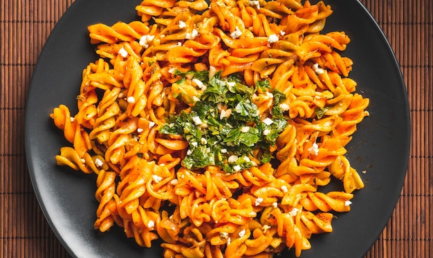 Macarrones de pasta rizada con salsa de tomate y gremolata en un plato oscuro redondo sobre una mesa