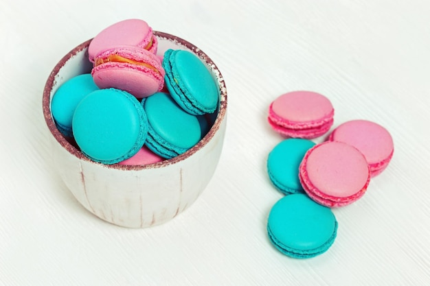 Macarrones rosas y azules en un tazón sobre fondo blanco de madera con espacio para copiar Fondo de alimentos