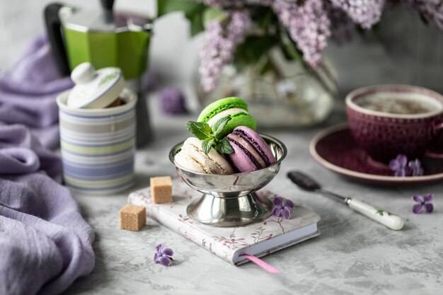 Macarrones con una taza de café sobre la mesa con un ramo de lilas.