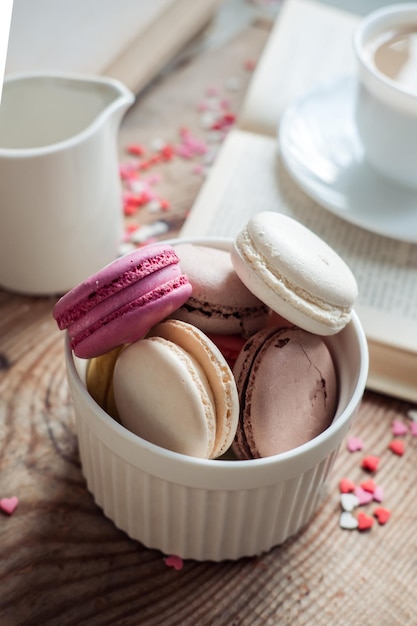 Macarrones en un tazón y una taza de café un libro sobre el fondo de pequeños corazones en una vista superior de fondo de madera