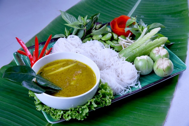 Macarronete de arroz tailandês comido com caril picante na bacia no fundo da folha da banana.