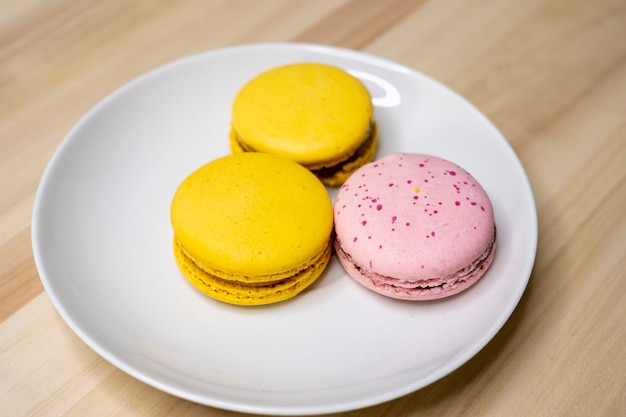 Macarrons amarelos e rosa em um prato branco na mesa de madeira