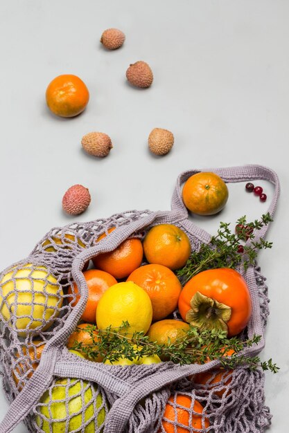 Maçãs de caqui e limão em sacos de malha reutilizáveis lychee cranberries e mandarinas na mesa