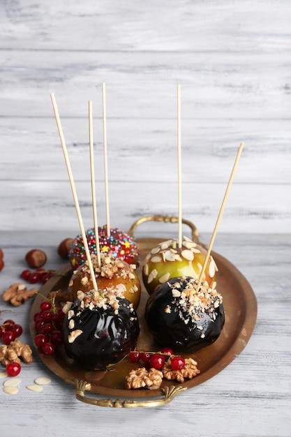 Maçãs de caramelo doce em palitos com bagas, na mesa de madeira