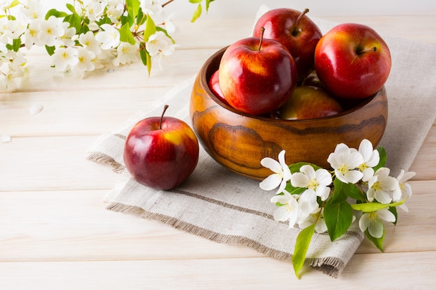 Maçãs frescas na tigela de madeira e flor de maçã