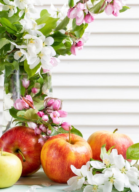 Foto maçãs perto e árvores de maçã florescem ramos em vaso de vidro sobre pano de fundo branco janela cega