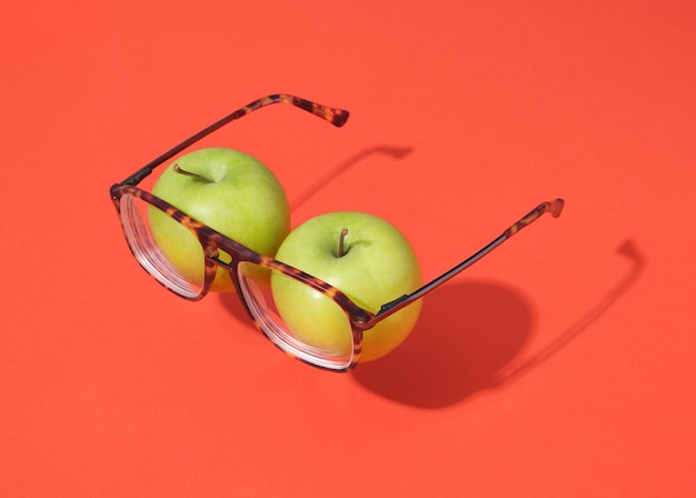 Maçãs verdes e óculos sobre fundo vermelho. As maçãs imitam os olhos. Correção de visão de ideia positiva.