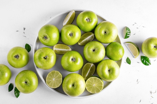 Maçãs verdes maduras frescas e limões suculentos na placa cerâmica branca