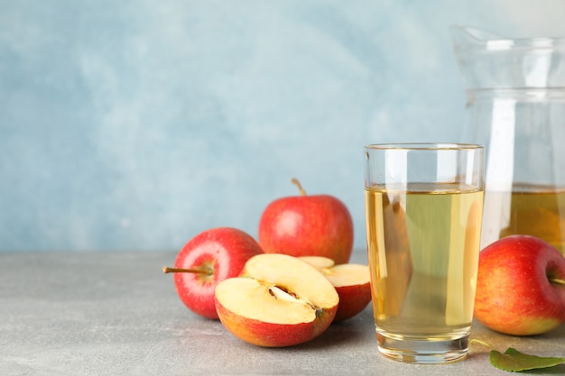 Maçãs vermelhas e copos com suco na mesa cinza