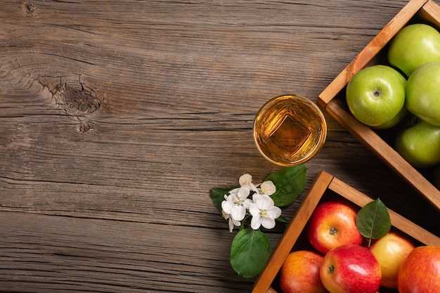 Maçãs vermelhas e verdes maduras em caixa de madeira com ramo de flores brancas e copo de suco fresco em uma mesa de madeira. Vista superior com espaço para seu texto.