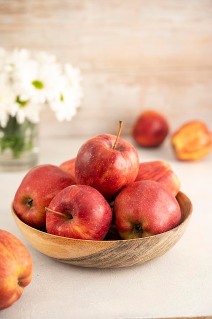 Maçãs vermelhas em tigela sobre fundo rústico de madeira Frutas frescas de maçã vermelha com flores