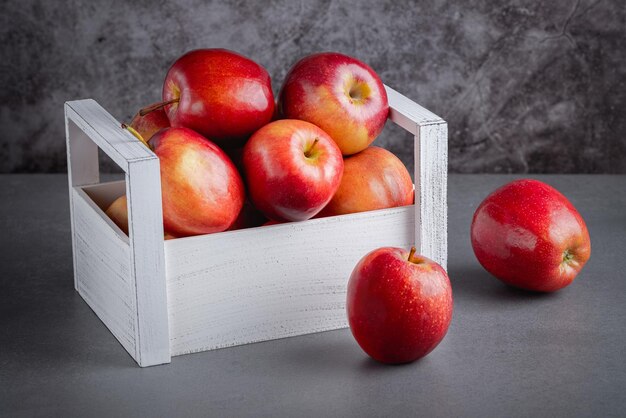 Maçãs vermelhas frescas em uma caixa de madeira em um fundo cinza Alimentos orgânicos