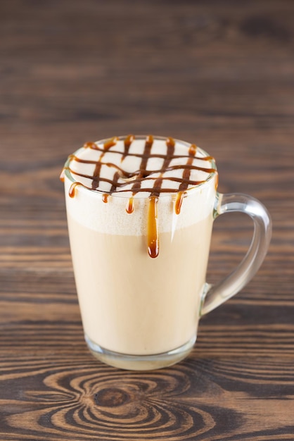 Macchiato de caramelo vegan com creme de coco em uma caneca de vidro sobre uma mesa de madeira.