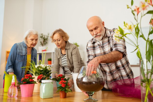 Macetas de flores. Hombre agradable agradable poniendo su mano en el jarrón mientras planta una flor