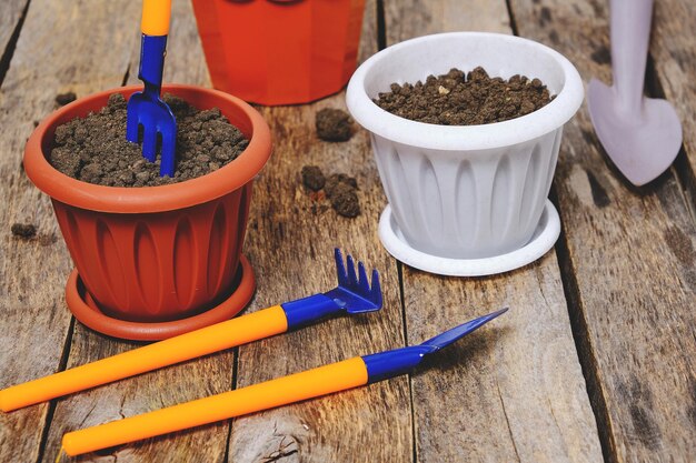 Macetas y herramientas decorativas de jardinería pala rastrillo y horca sobre un fondo de madera