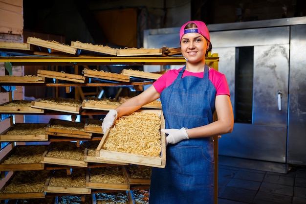 Machen Sie die Nudeln. Teigwarenfabrik. Spaghetti-Produktion. Rohe Nudeln. Arbeiter mit einer Schachtel Nudeln. Mädchen arbeitet in der Herstellung von Nudeln